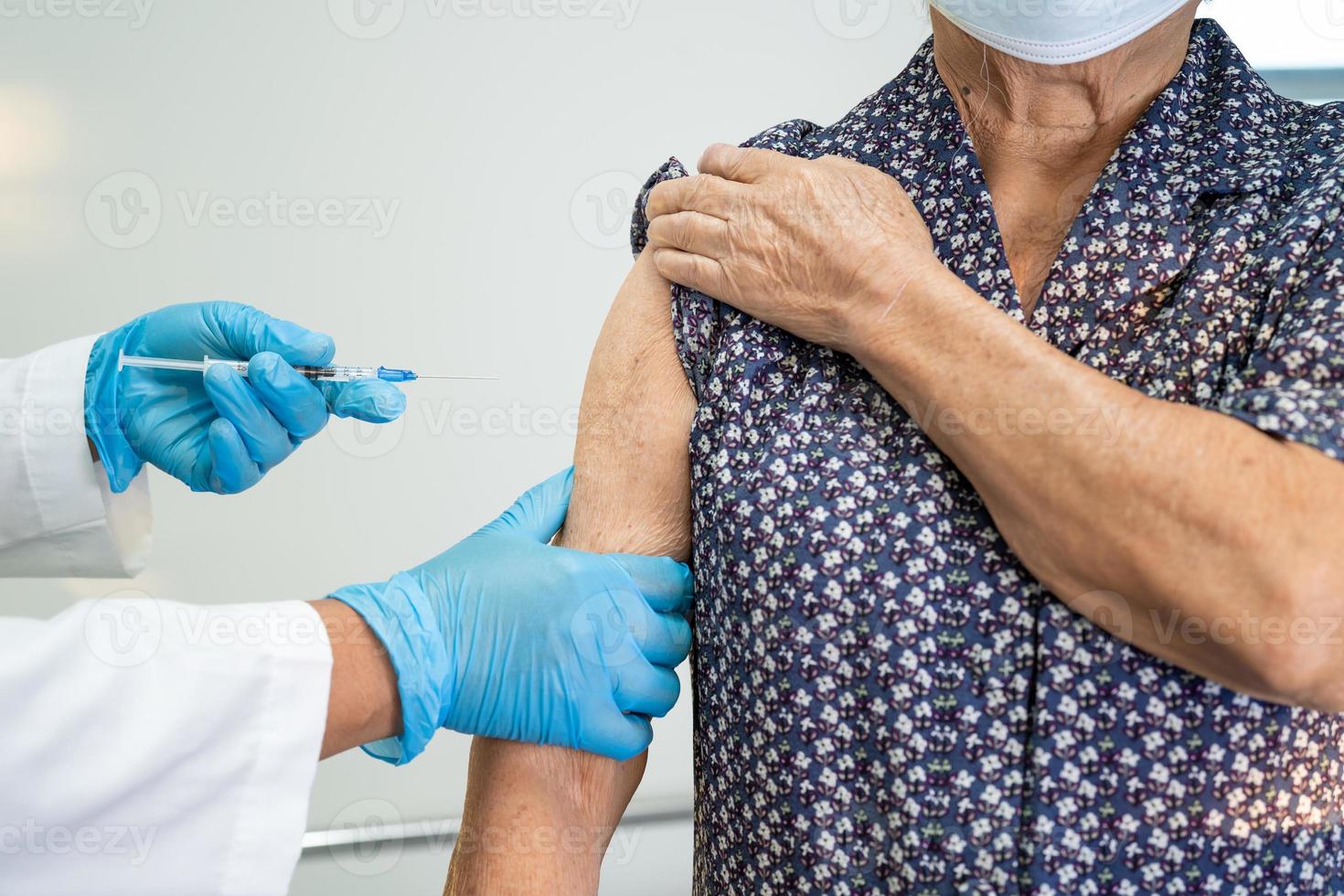 Elderly Asian senior woman wearing face mask getting covid-19 or coronavirus vaccine by doctor make injection. photo