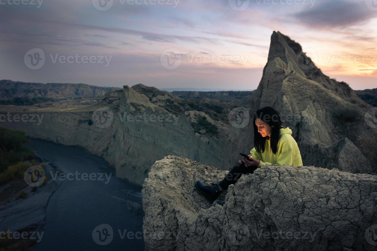 Caucasian woman sits on the cliff and looks to smartphone with river and Mijniskure landscape photo