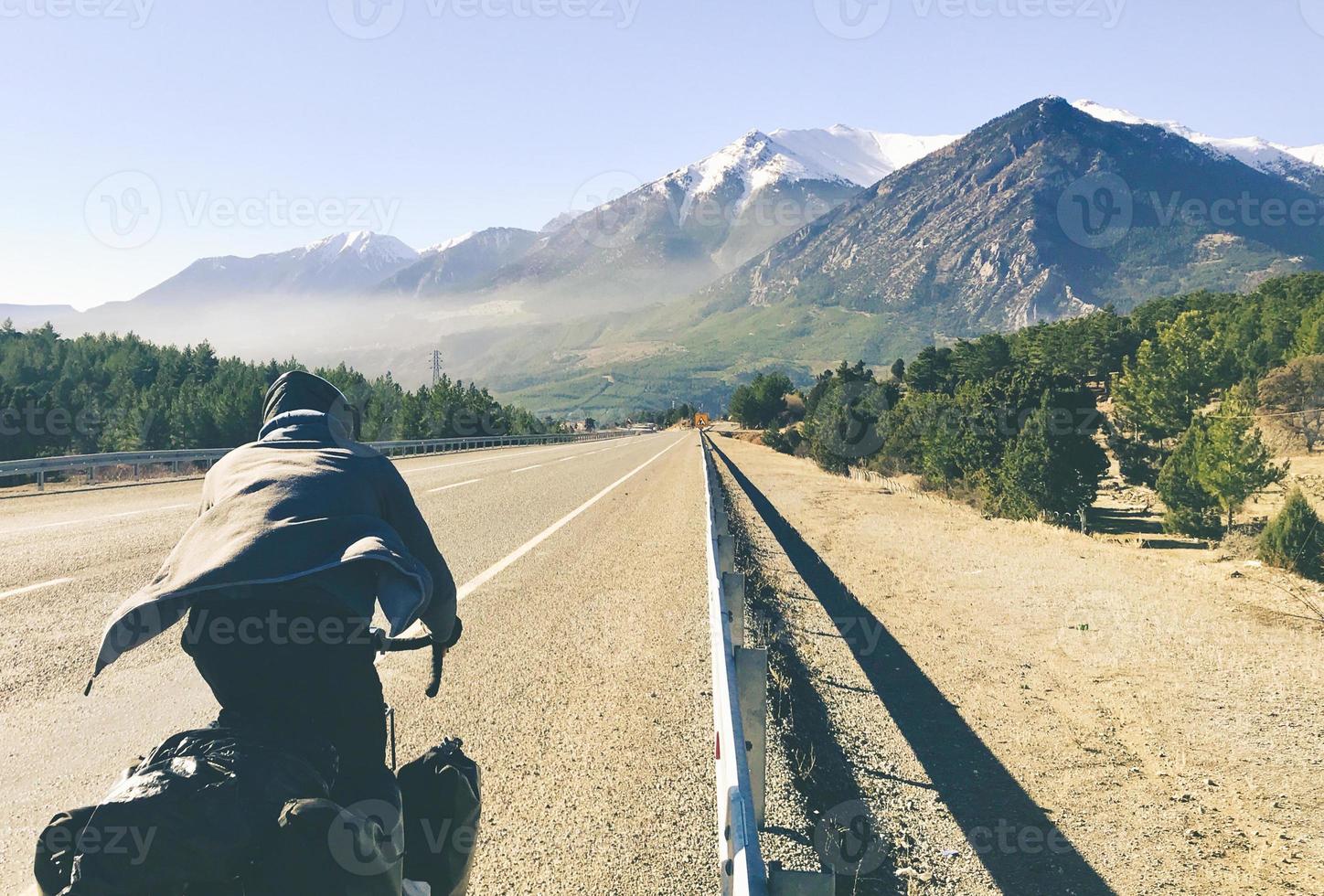 Back view close up cyclist on bicycle touring bicycle rides fast downhill outdoors in scenic mountains photo