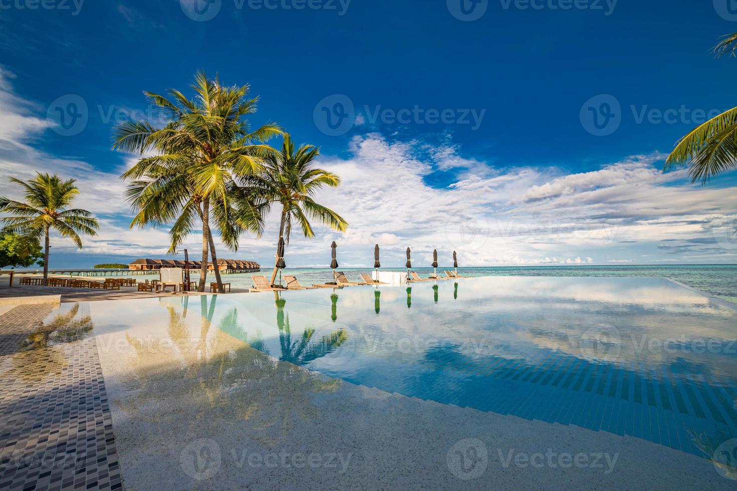 Outdoor tourism landscape. Luxurious beach resort with swimming pool and beach chairs or loungers under umbrellas with palm trees and blue sky. Summer travel and vacation background concept photo