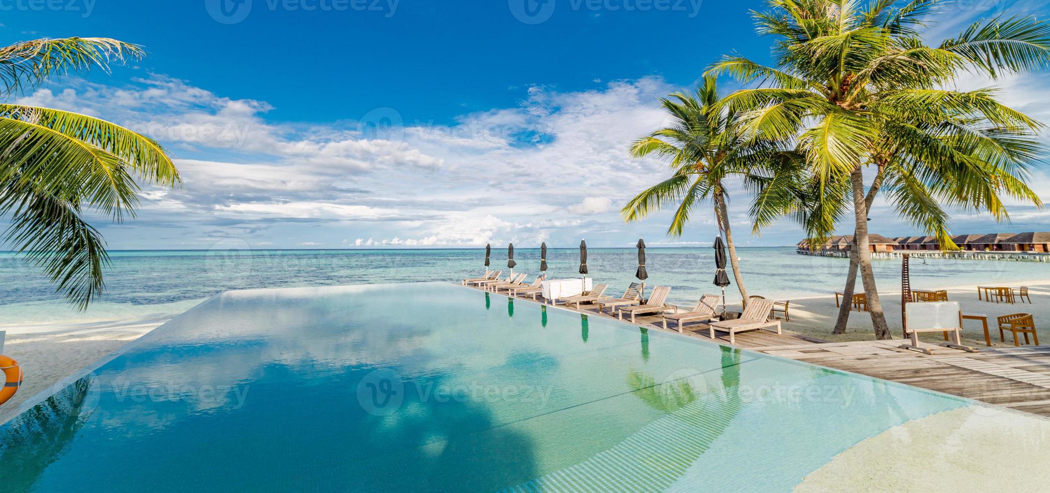 Outdoor tourism landscape. Luxurious beach resort with swimming pool and beach chairs or loungers under umbrellas with palm trees and blue sky. Summer travel and vacation background concept photo