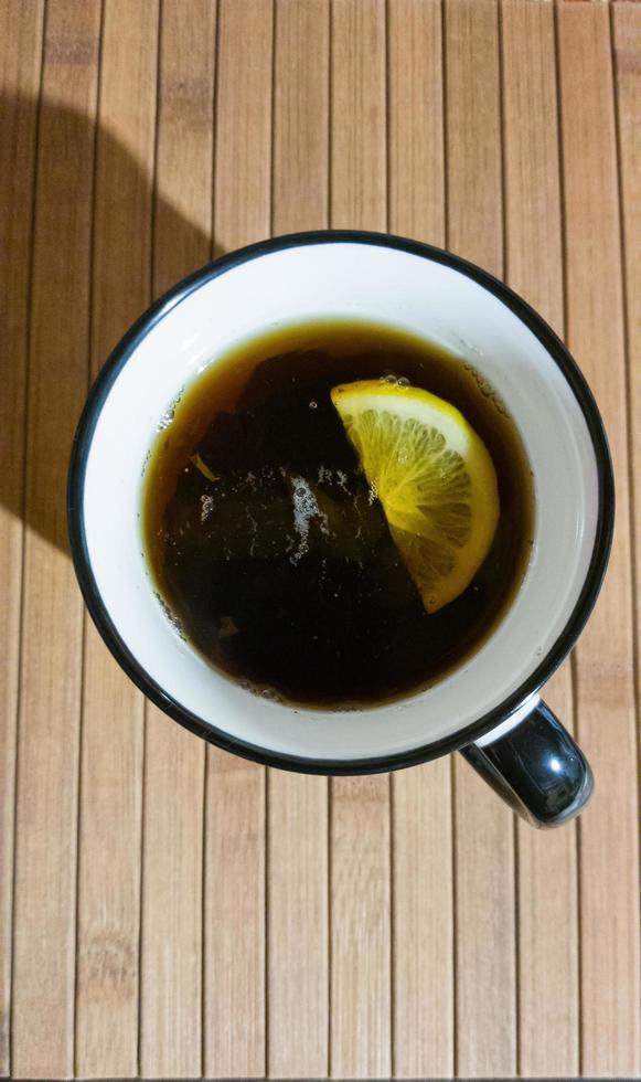 White mug with black tea and lemon slice on wooden background photo