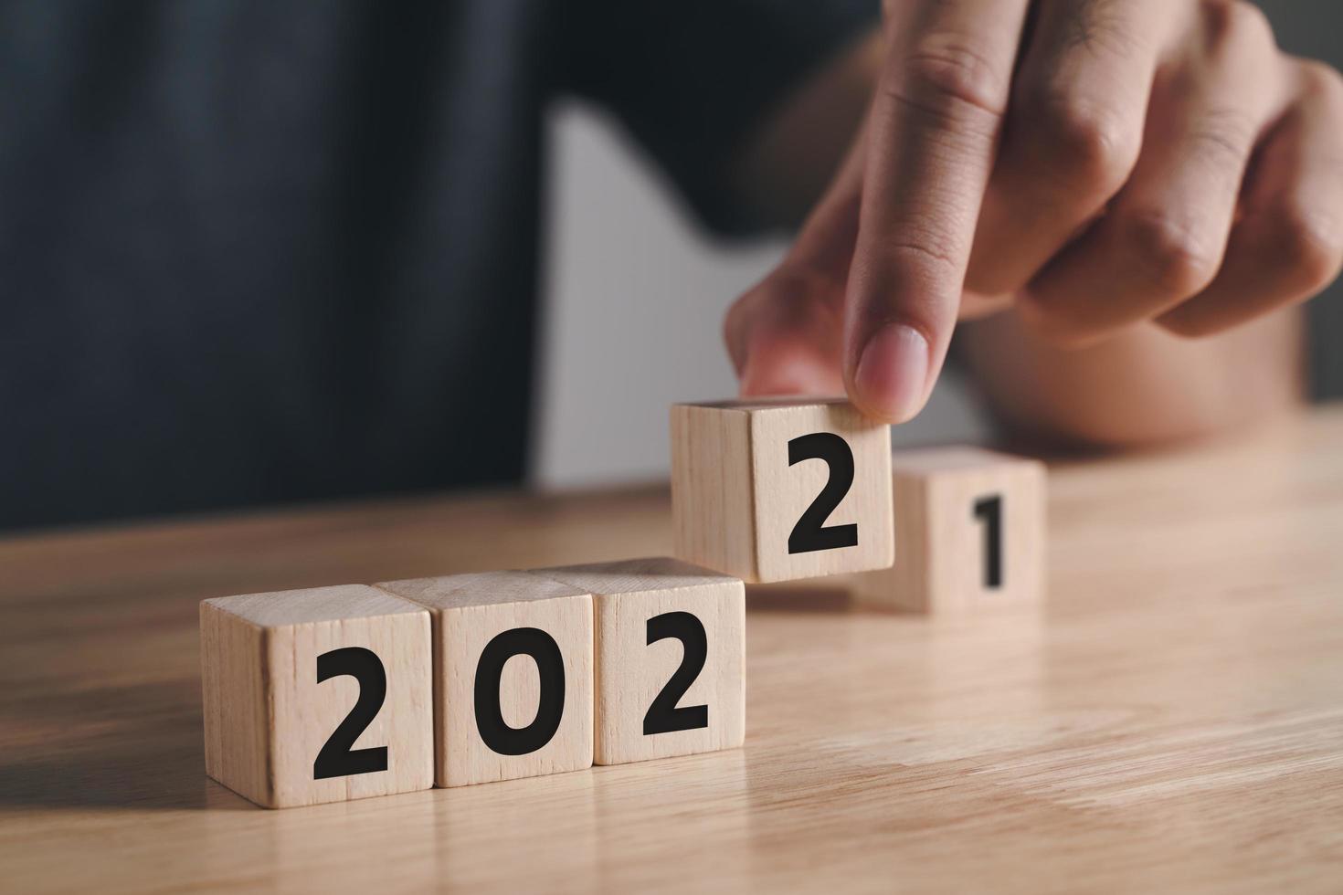 Mano de hombre poniendo un bloque de cubo de madera para cambiar el año 2021 al año 2022 en la mesa de madera con espacio de copia. comienzo del año 2022. feliz año nuevo concepto. foto