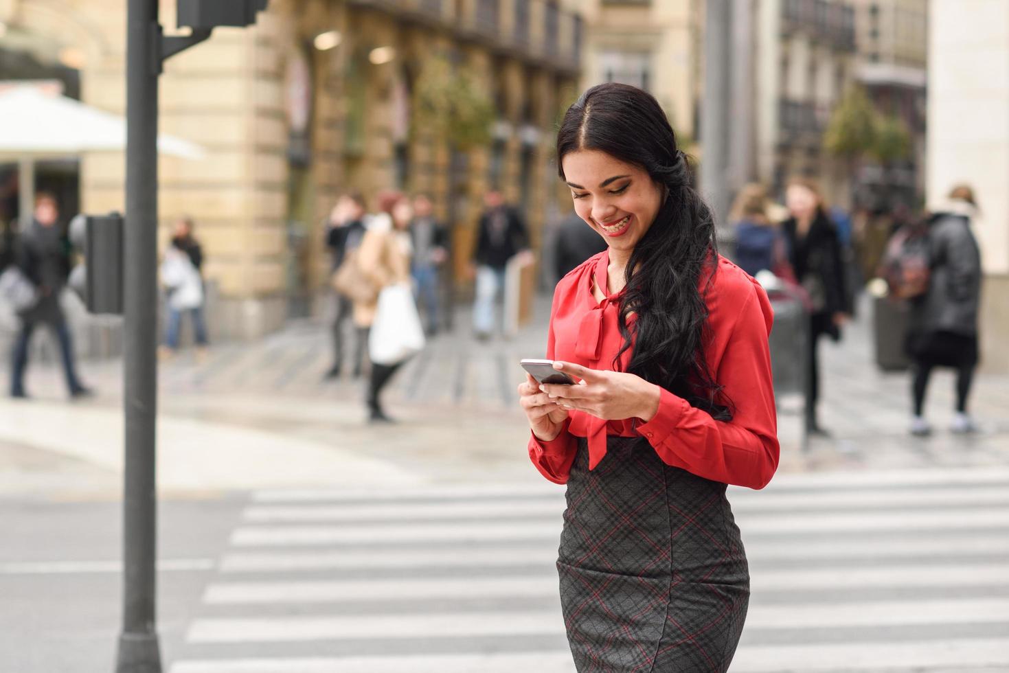 Azafata hispana en fondo urbano mirando su teléfono móvil foto