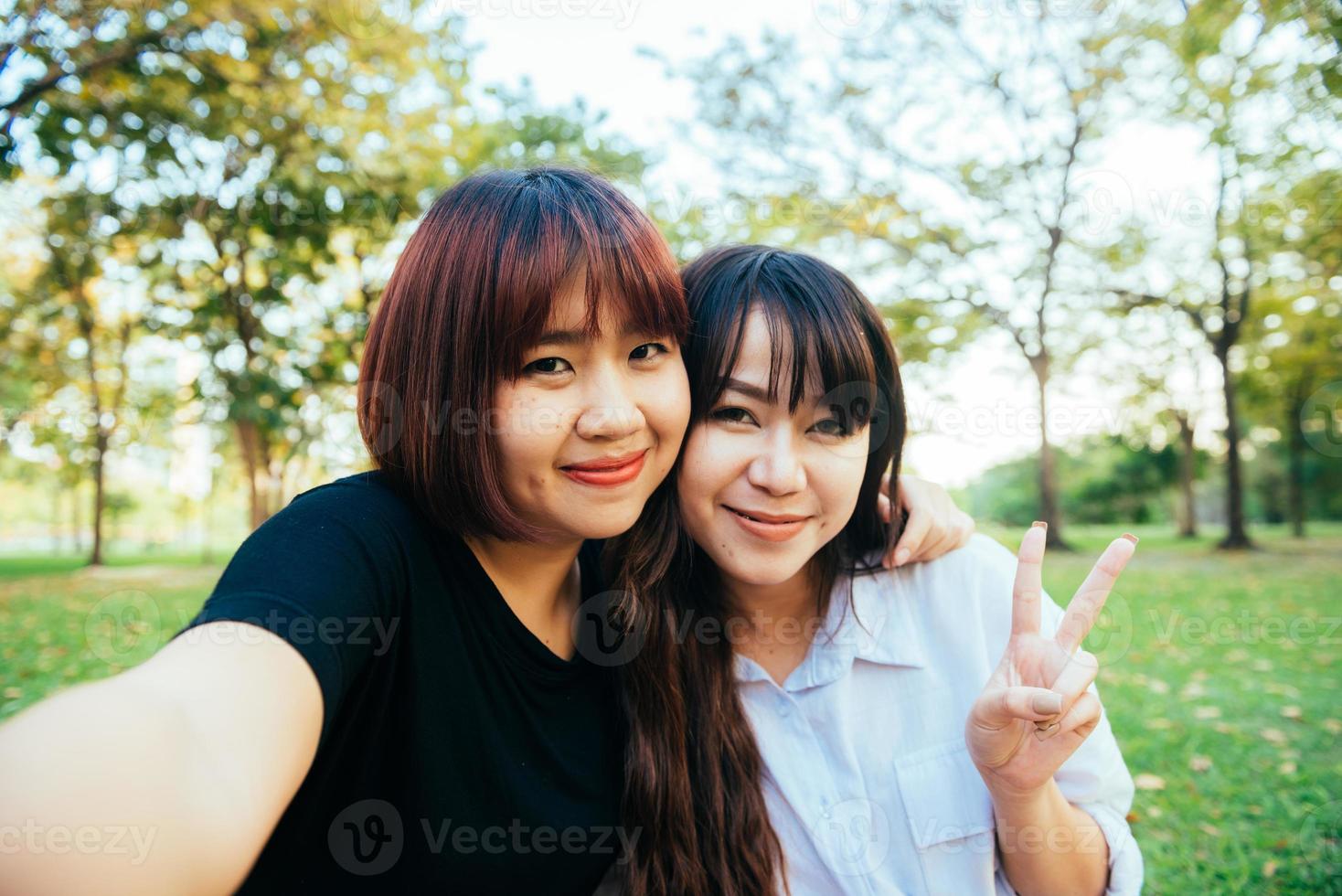 Two beautiful happy young asian women friends having fun together at park and taking a selfie. Happy hipster young asian girls smiling and looking at camera. Lifestyle and friendship concepts. photo