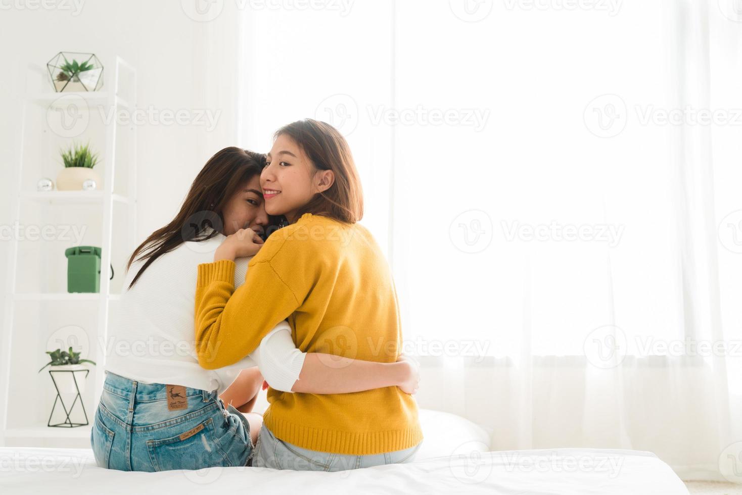 Back view of women lesbian happy couple waking up in morning, sitting on bed, stretching in cozy bedroom, looking through window. Funny women after wakeup. LGBT Lesbian couple together indoors concept photo