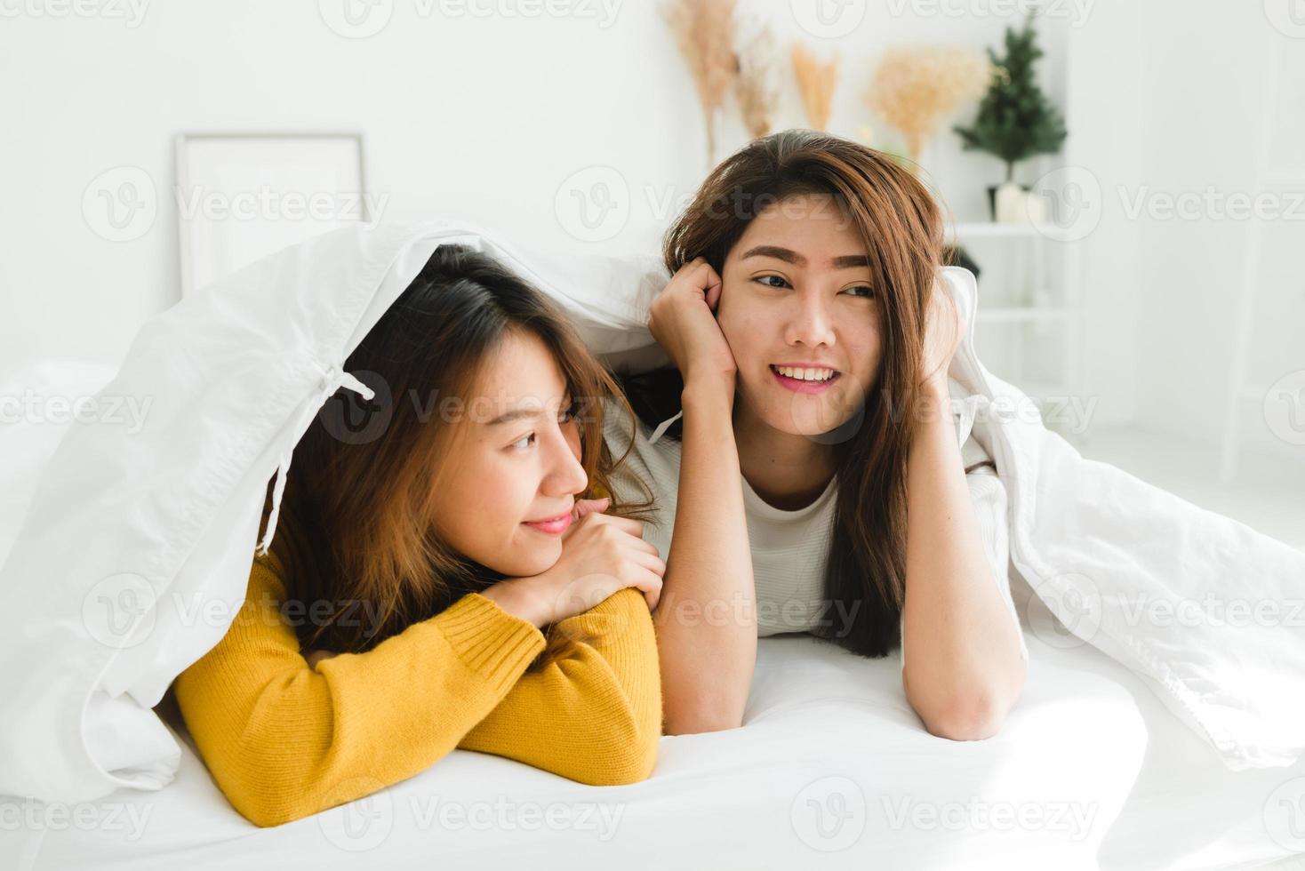 Top view of beautiful young asian women lesbian happy couple showing surprise and looking at camera while lying in bed under blanket. Funny women after wake up. Lesbian couple together indoors concept photo