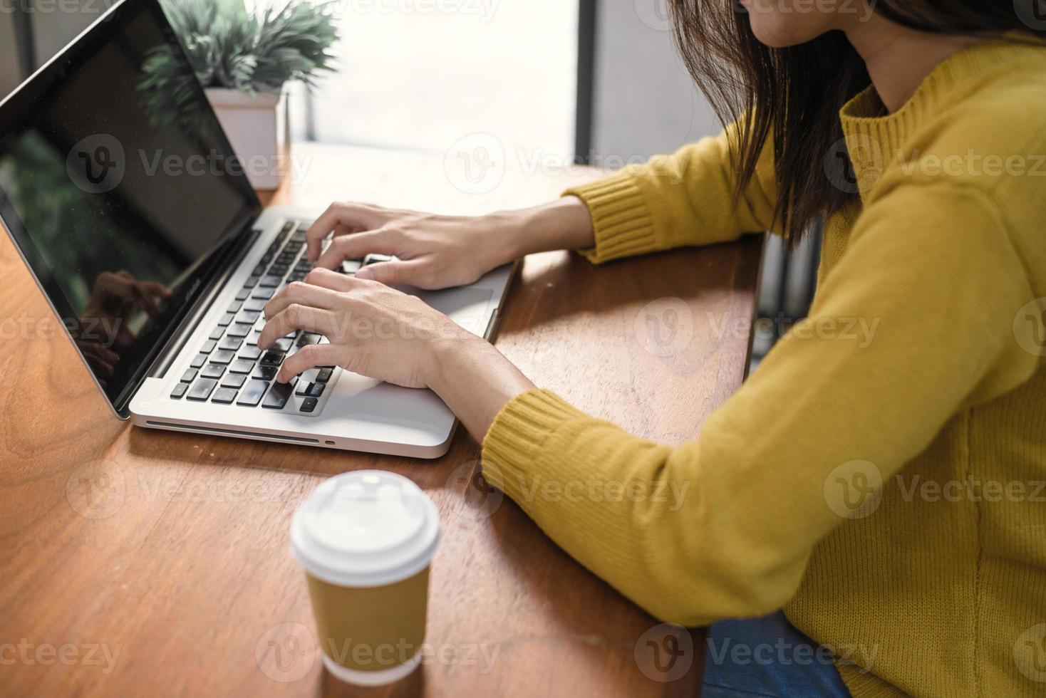 Conceptos de tecnología empresarial: estilo de vida digital que trabaja fuera de la oficina. manos de mujer escribiendo ordenador portátil con pantalla en blanco sobre la mesa en la cafetería. maqueta de pantalla de portátil en blanco para mostrar el diseño foto