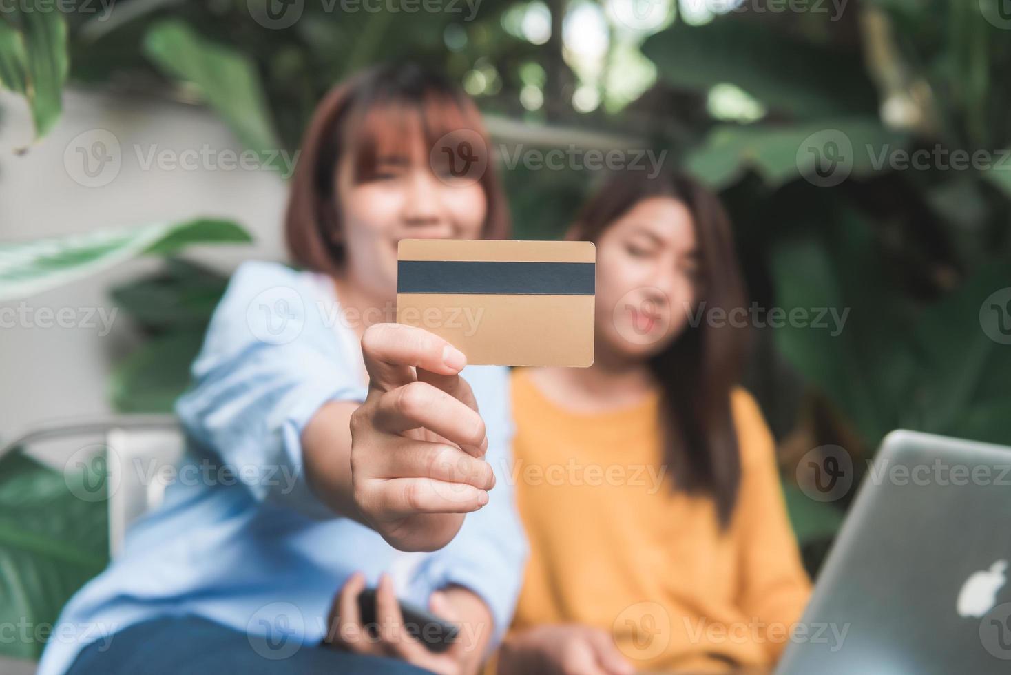 Close up of a couple young Asian women using her credit card while they do shopping online with her laptop. Young women shopping online in the garden holding her credit card. Shopping online concept. photo
