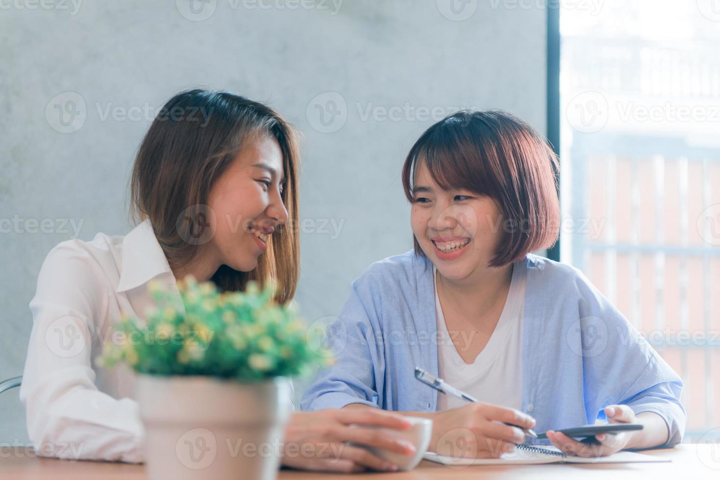 Two young business women sitting at table in cafe. Asian women using laptop and cup of coffee. Freelancer working in coffee shop. Working outside office lifestyle. One-on-one meeting. photo