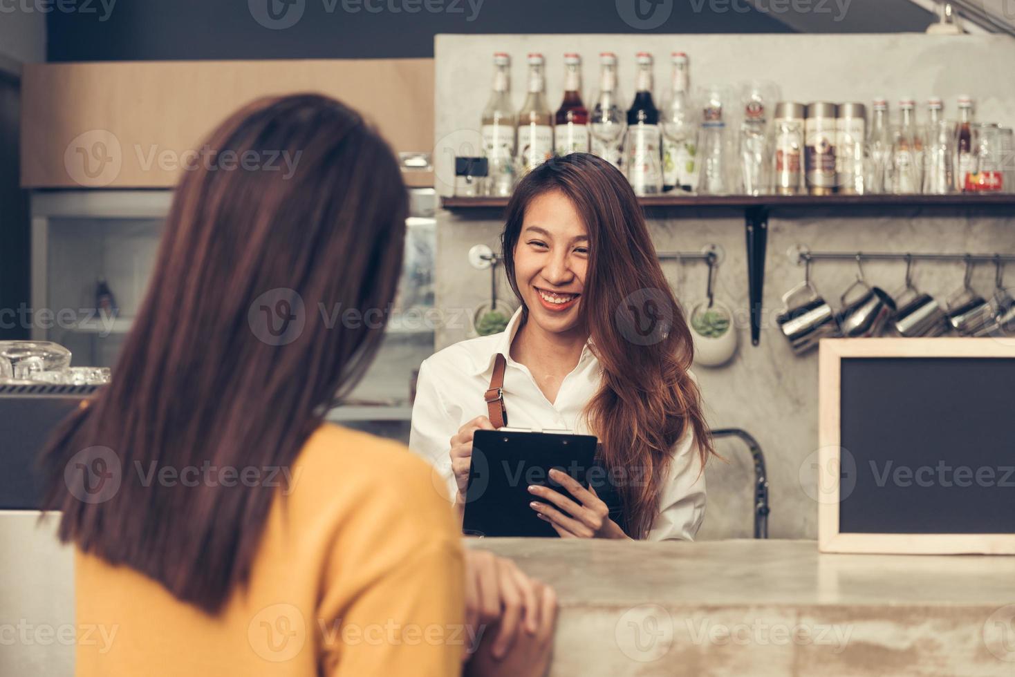 Close up of Young Asian female coffee shop owner taking the order from her client with a warm welcome smile in her small coffe shop. Young Woman get order of coffee from her client. Foods and drinks. photo