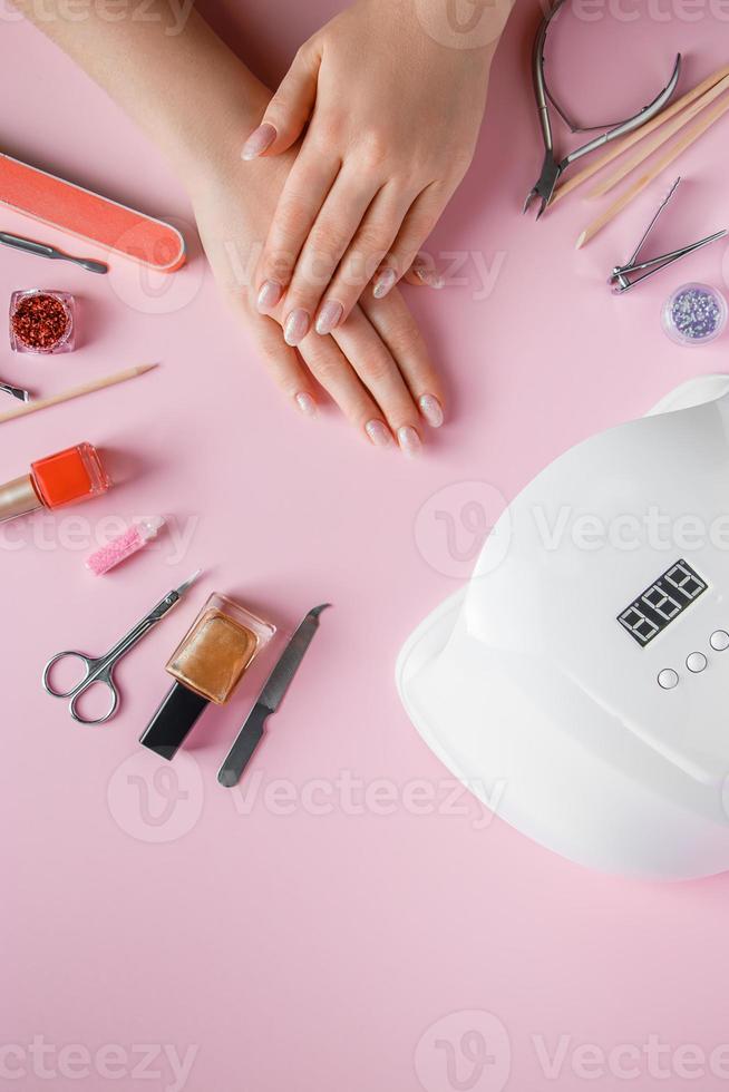 procedimiento de spa para el cuidado de las uñas en un salón de belleza. manos femeninas y herramientas para manicura sobre fondo rosa. foto