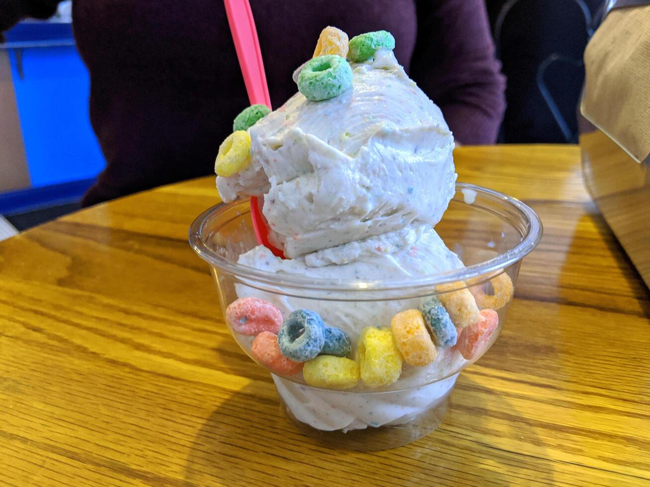 helado sabor vainilla y anillo colorido patrón de postre congelado en taza blanca mano sujetando sobre mesa de madera. foto