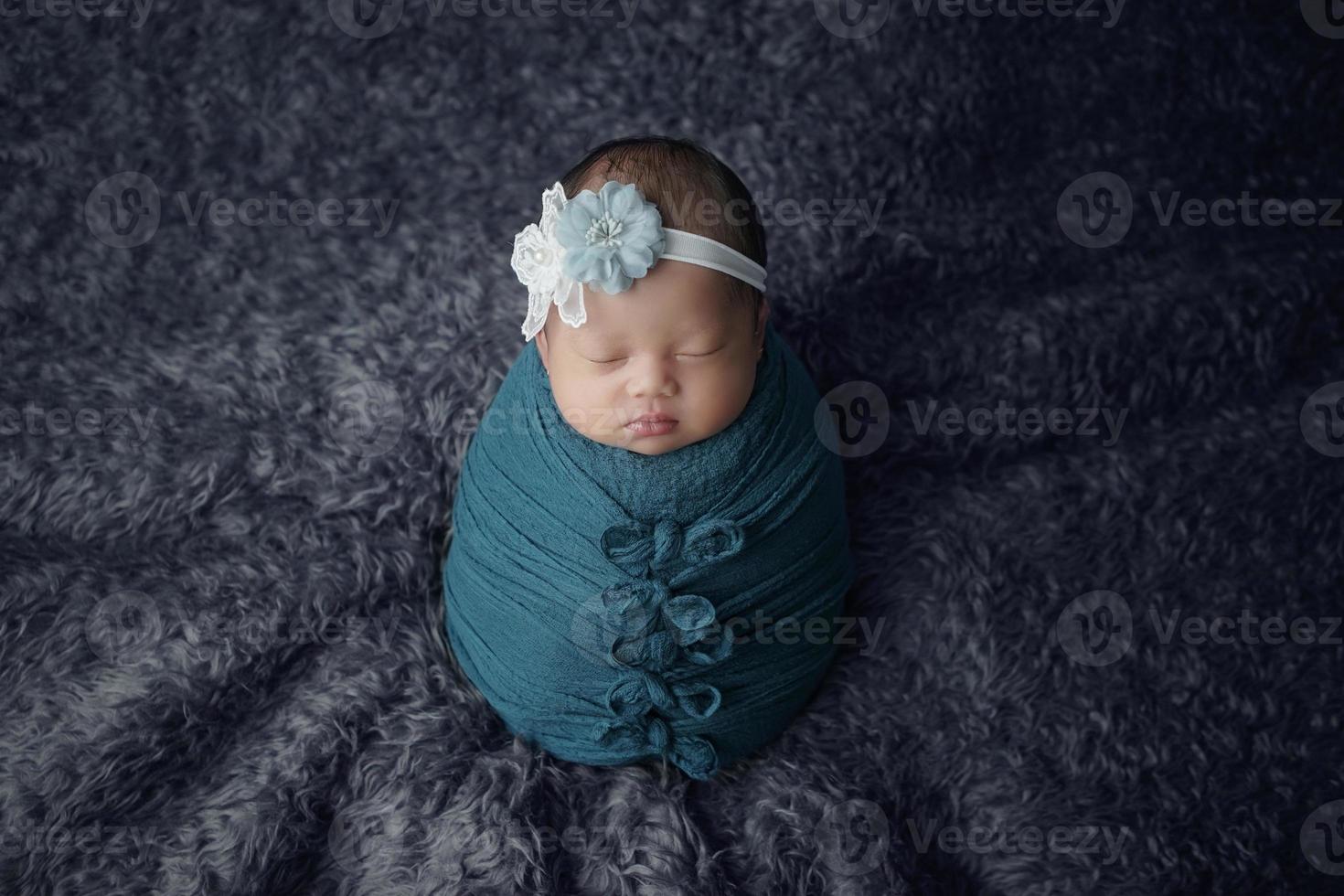 Little newborn baby enveloped in blue scarf with a bandage on his head lies on a soft blanket photo