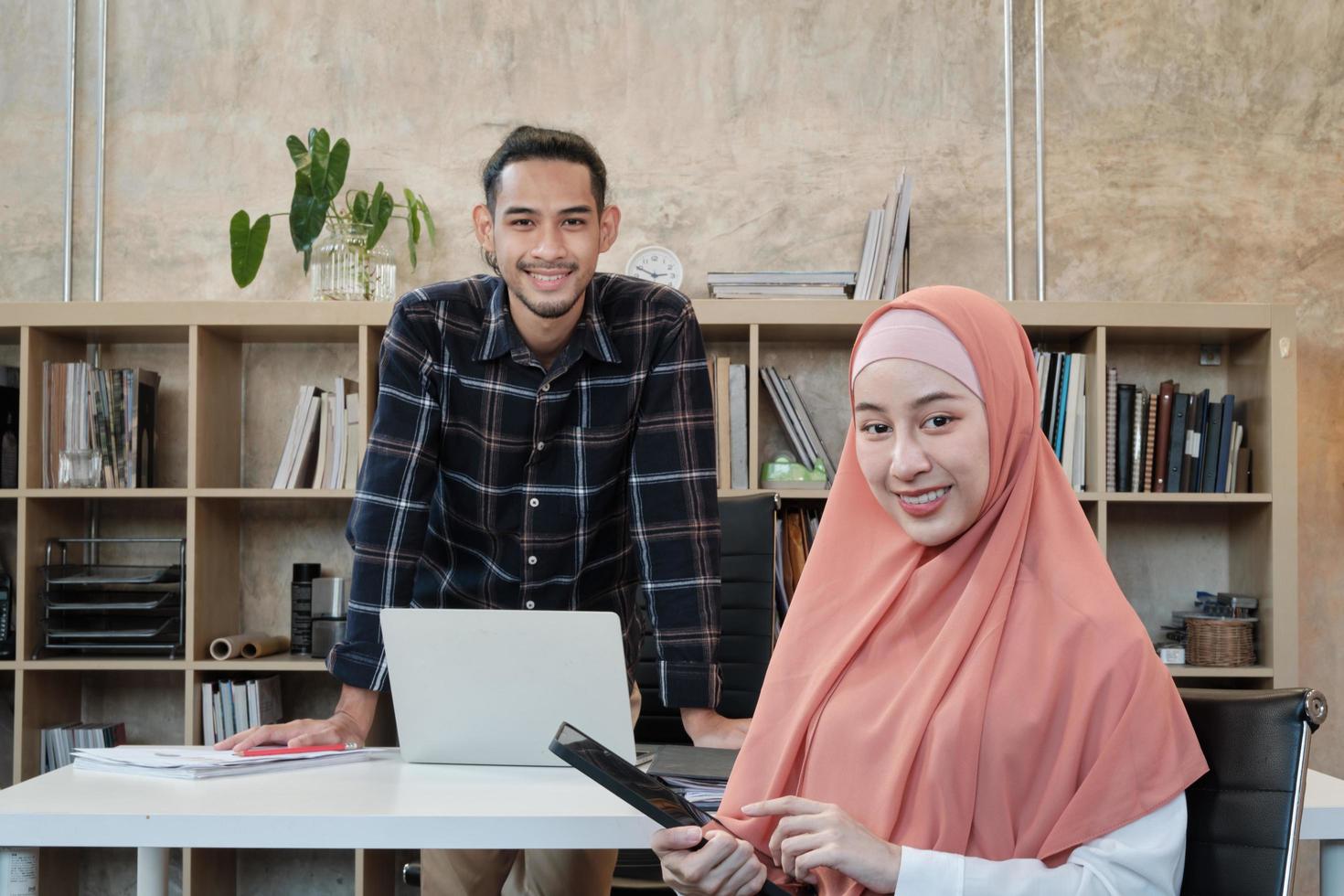 Portrait of entrepreneur of business startup, young male and beautiful female owner, two partners Islamic people, looking at camera, smiles happily in small e-commerce workplace office. photo