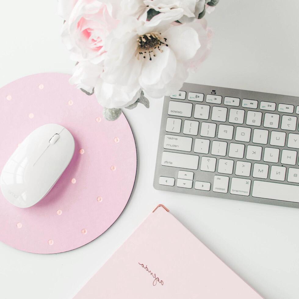 espacio de trabajo blanco con cuaderno rosa claro y flor blanca con café en la mesa blanca. foto