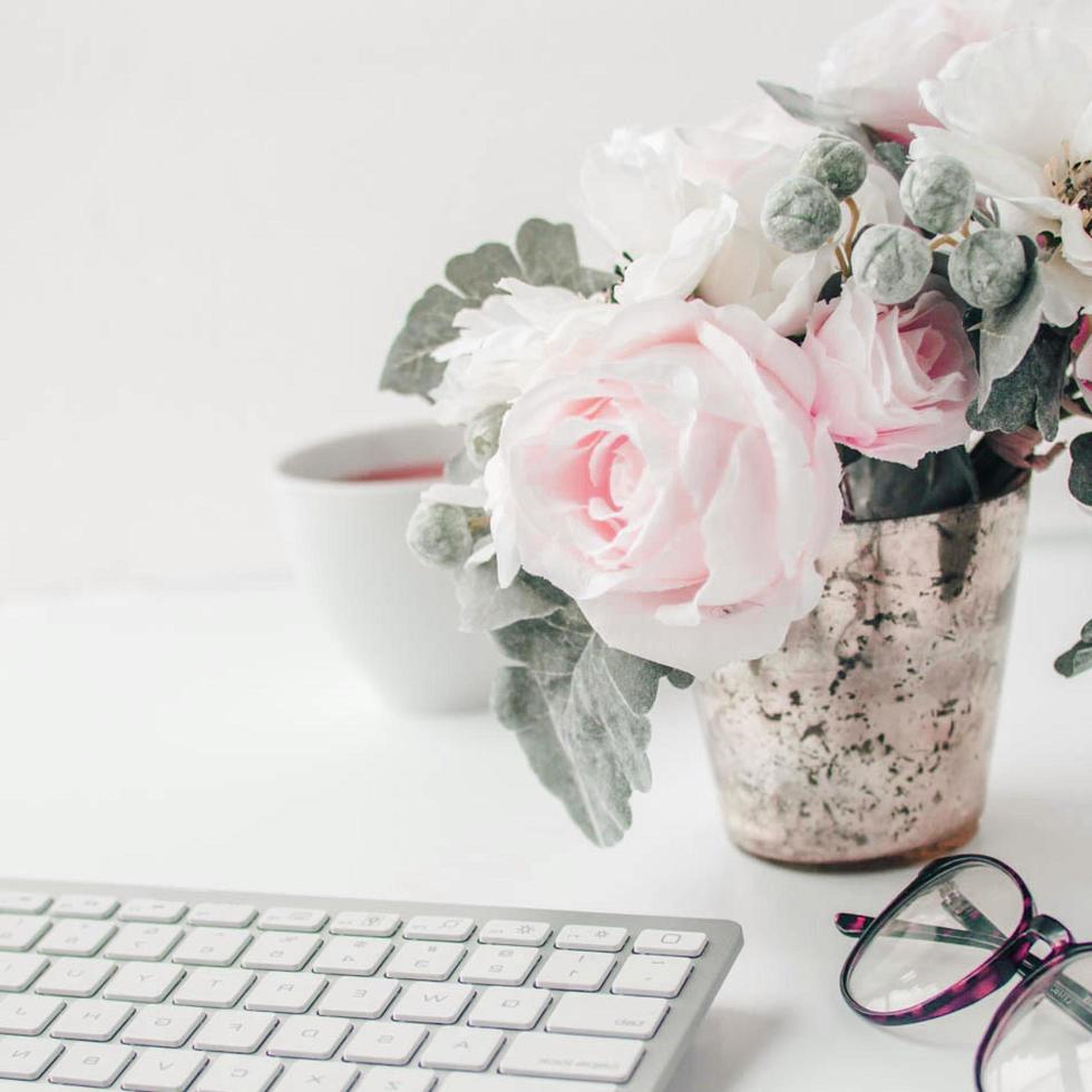 white workspace with light pink note book and white flower with coffee on white table. photo