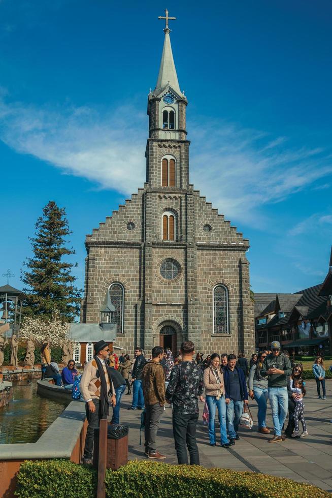 Gramado, Brazil - July 21, 2019. Church facade with steeple and people on a little square with sunny day at Gramado. A cute european-influenced town highly sought after by tourists. photo