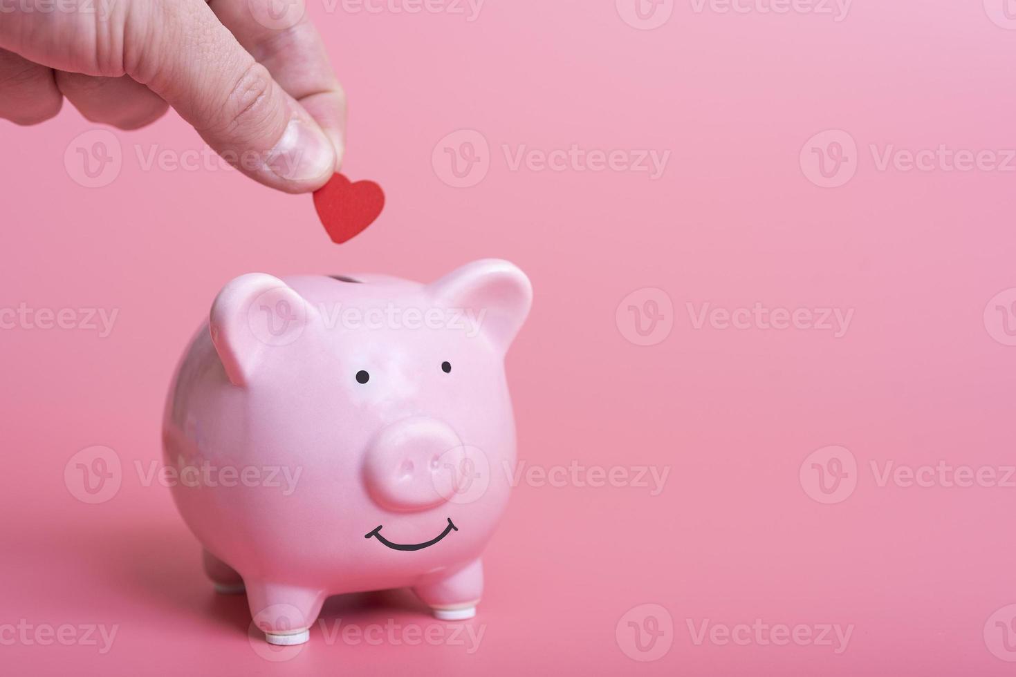 close-up of a manual deposit red heart in a piggy bank on a pink background photo