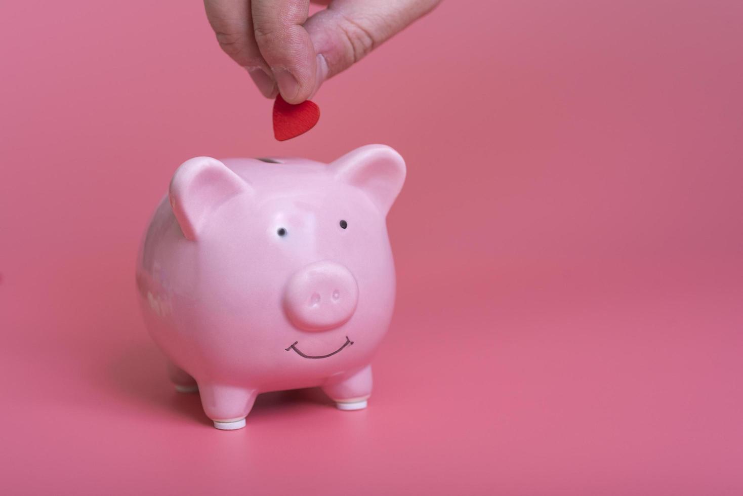 close-up of a manual deposit red heart in a piggy bank on a pink background photo