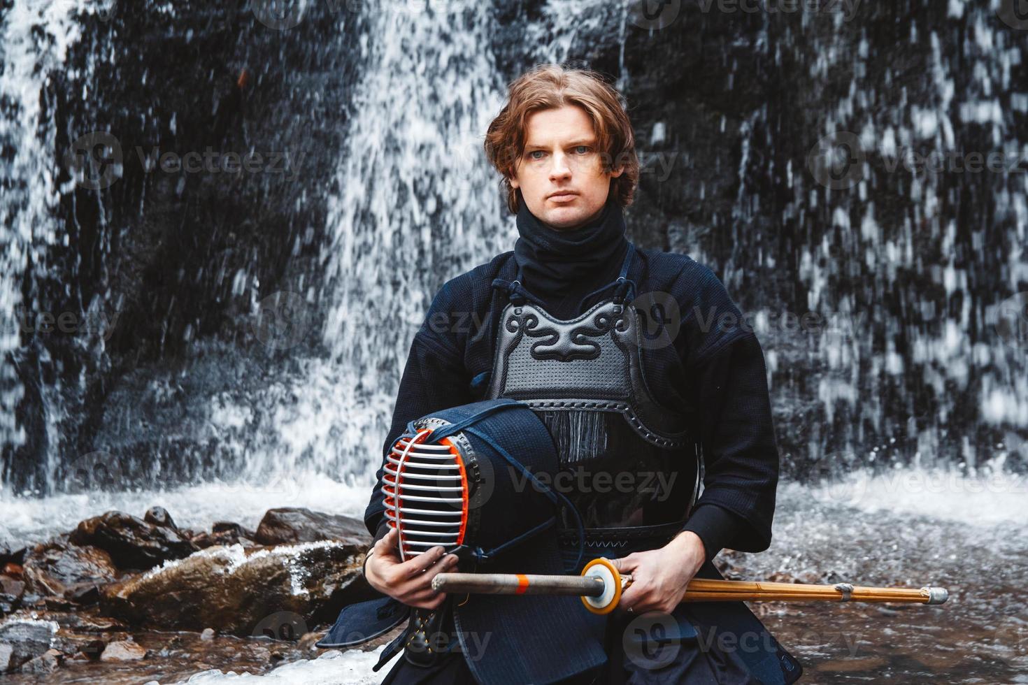 Man practicing kendo with bamboo sword on waterfall background photo