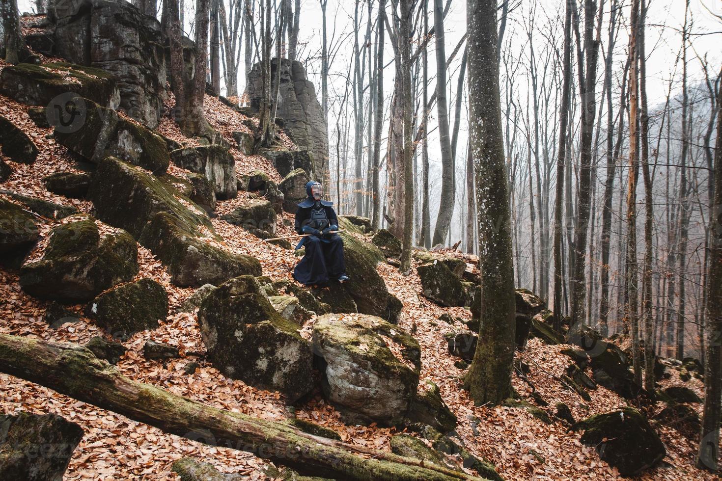 Man practicing kendo with shinai bamboo sword on rocks and forest background photo