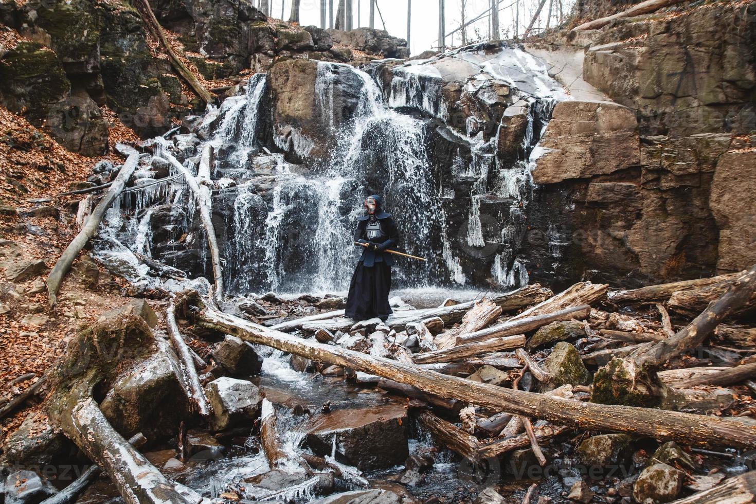 Man practicing kendo with bamboo sword on waterfall, rocks and forest background photo