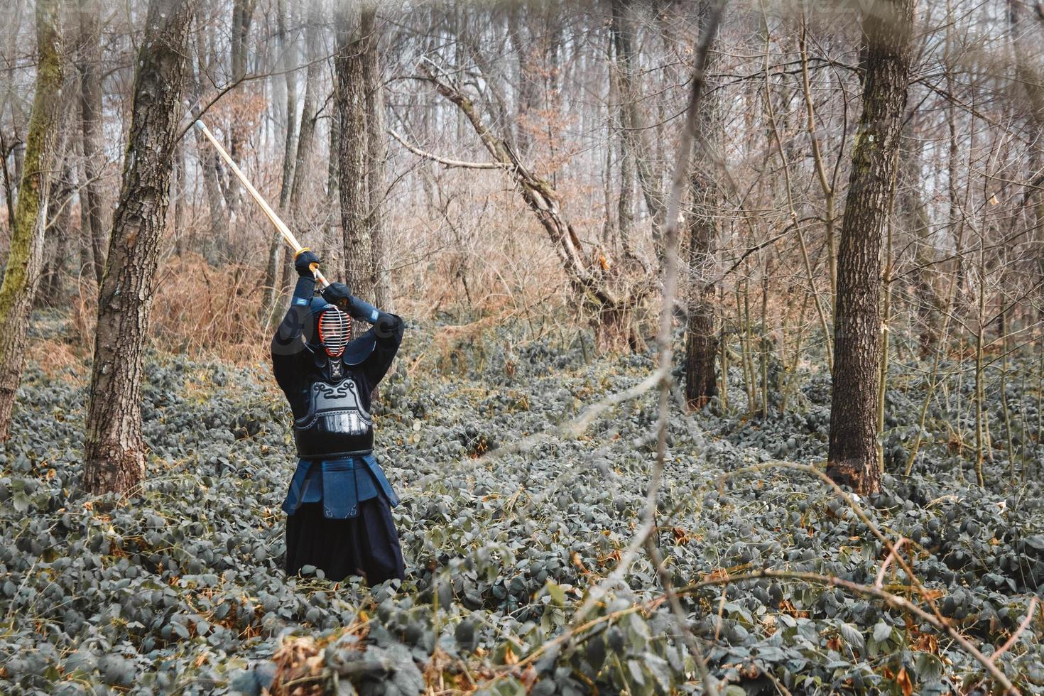 Hombre practicando kendo con espada de bambú shinai sobre fondo de bosque foto