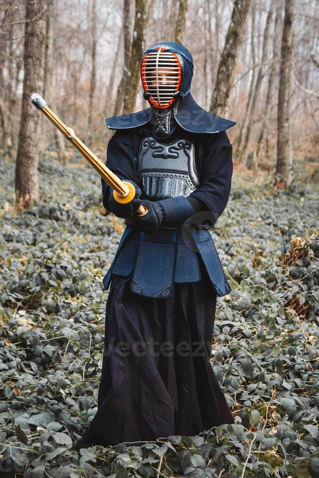 Hombre practicando kendo con espada de bambú shinai sobre fondo de bosque foto