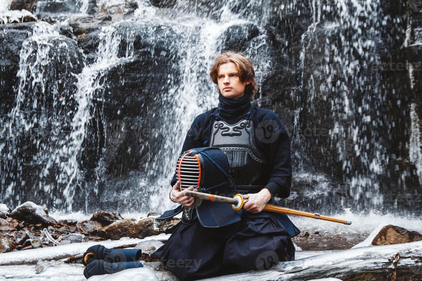 Man practicing kendo with bamboo sword on waterfall background. Place for text or advertising photo