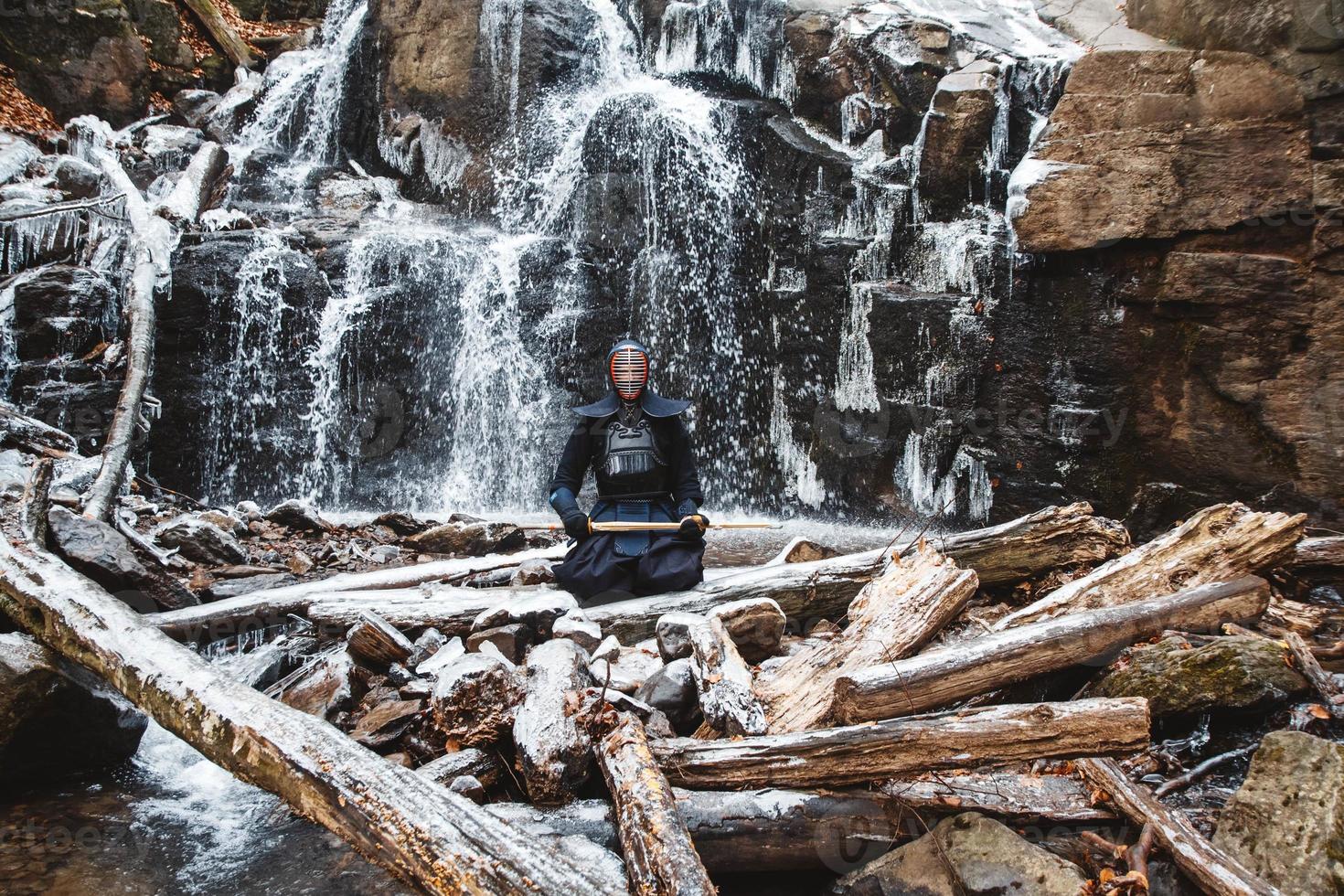 Man practicing kendo with bamboo sword on waterfall background photo