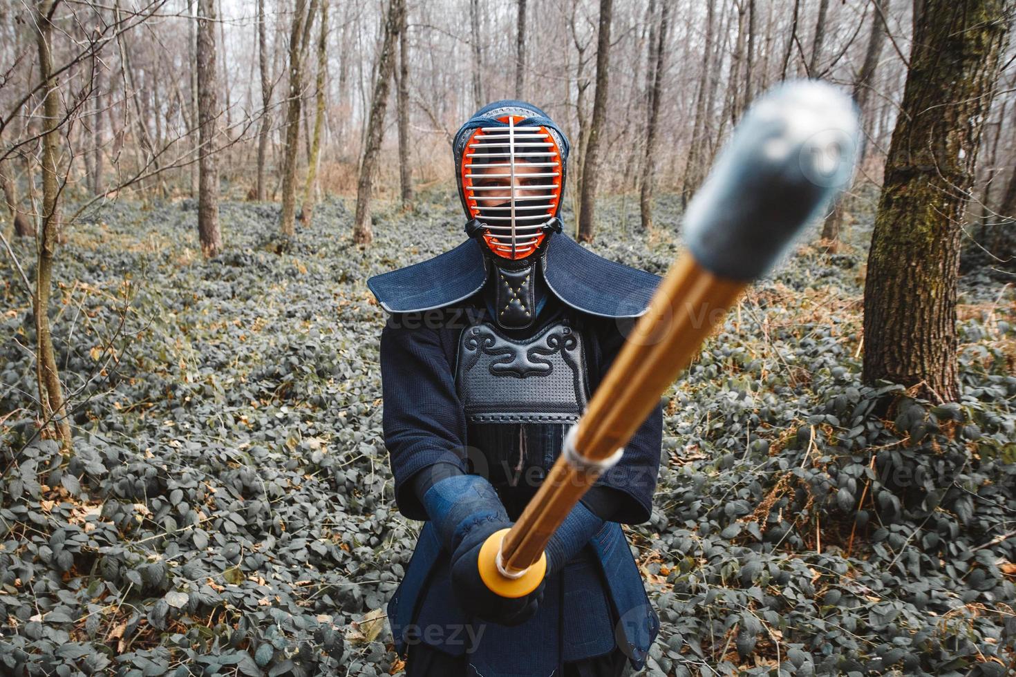 Hombre practicando kendo con espada de bambú shinai sobre fondo de bosque foto