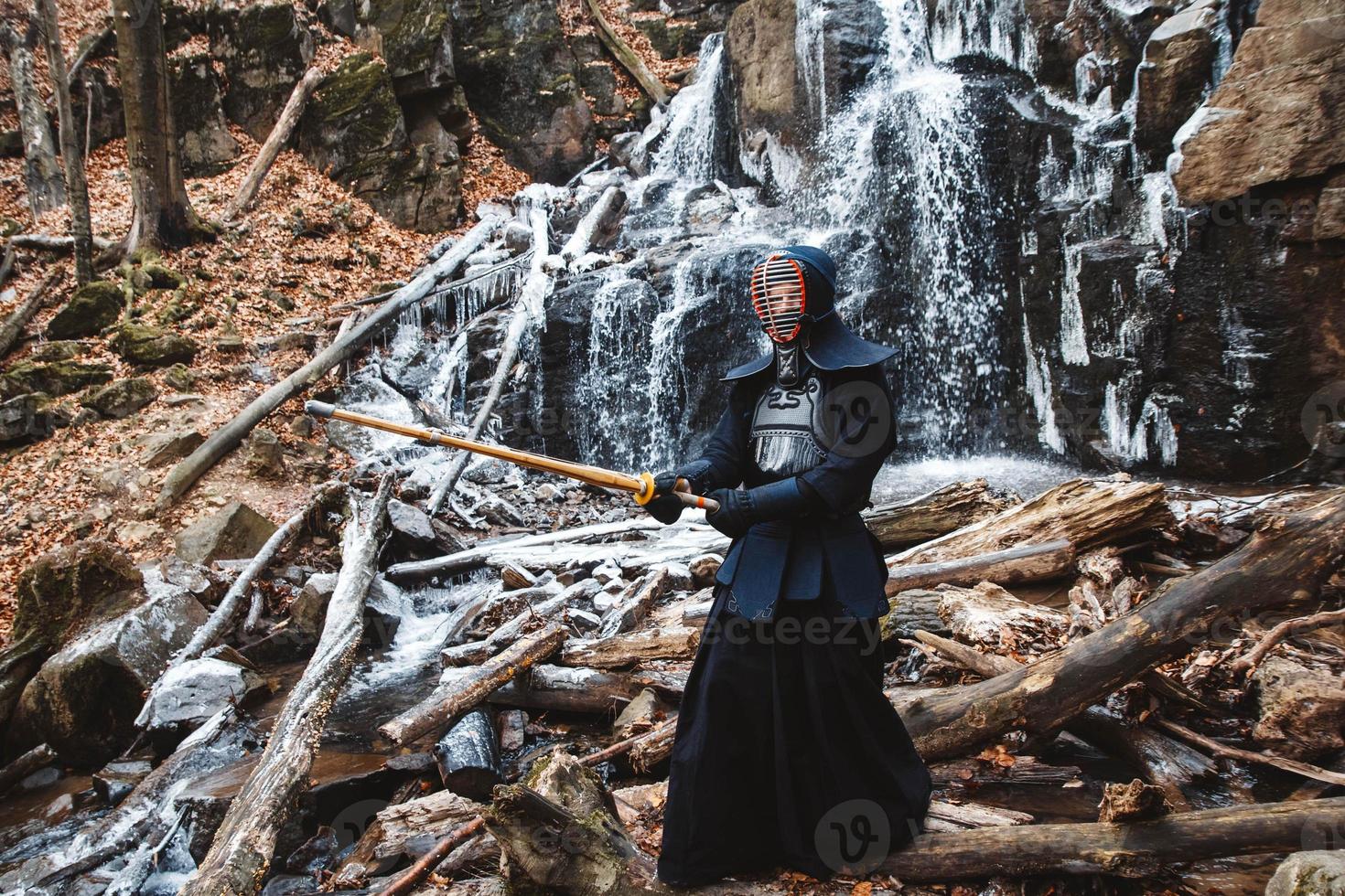 Man practicing kendo with bamboo sword on waterfall, rocks and forest background photo