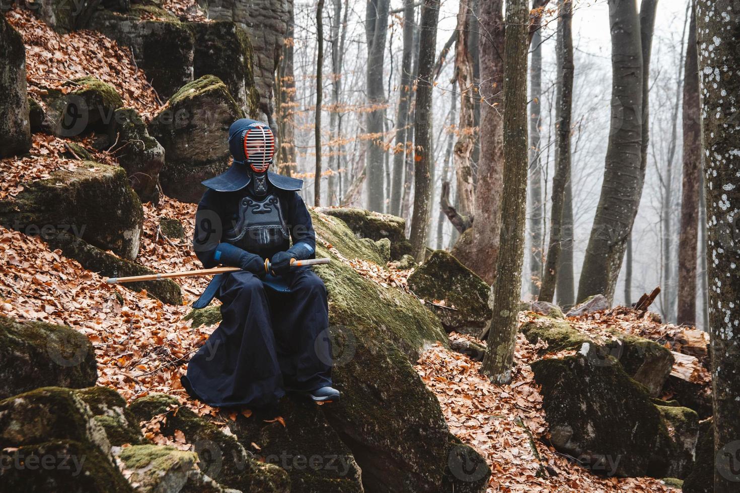 Man practicing kendo with shinai bamboo sword on rocks and forest background photo