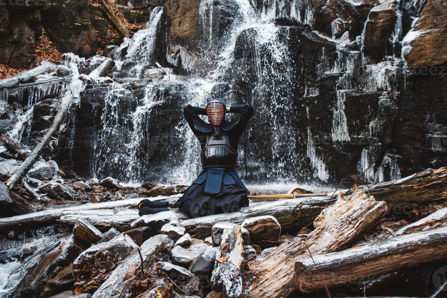 Man practicing kendo with bamboo sword on waterfall background photo