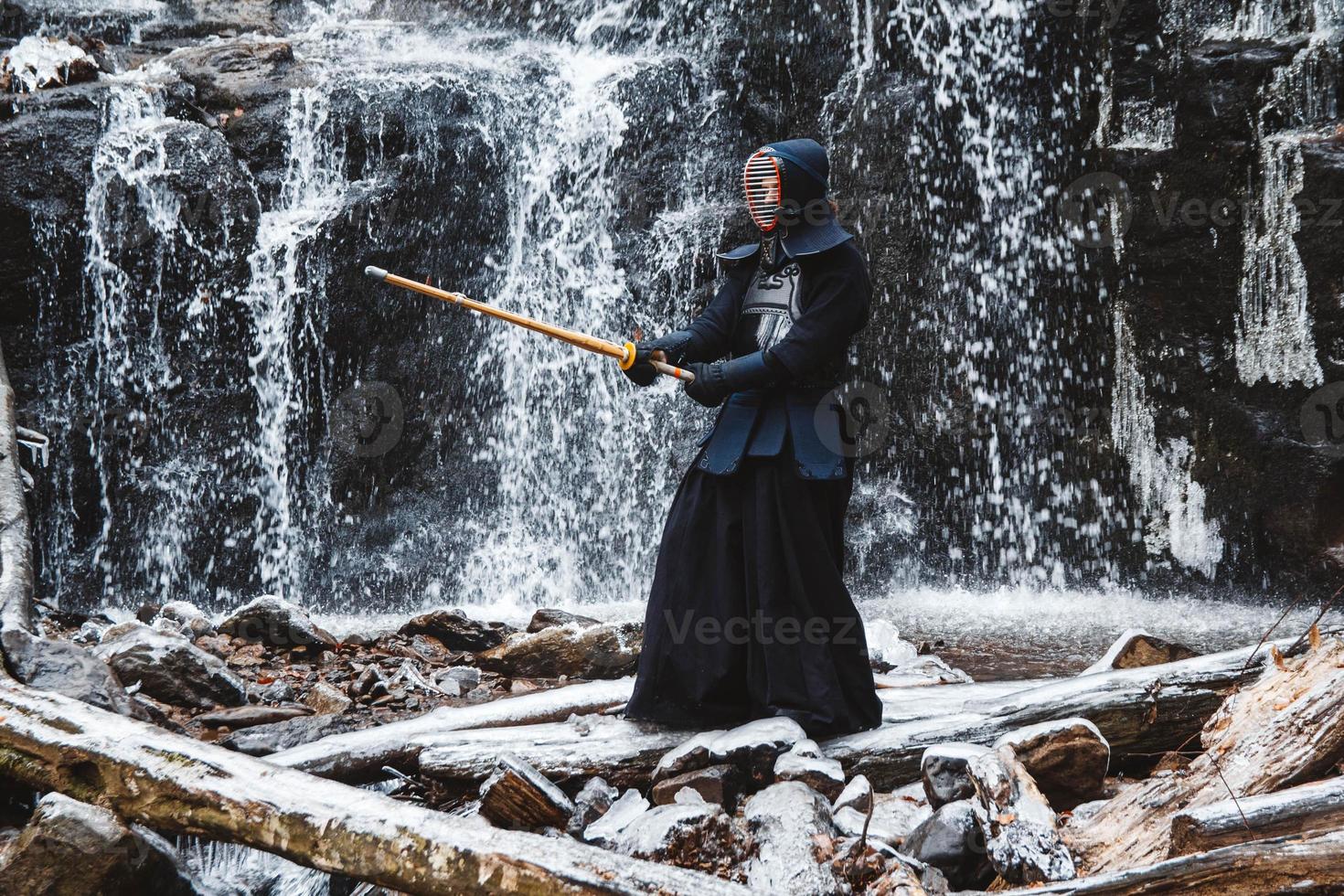 Hombre practicando kendo con espada de bambú sobre fondo de cascada foto