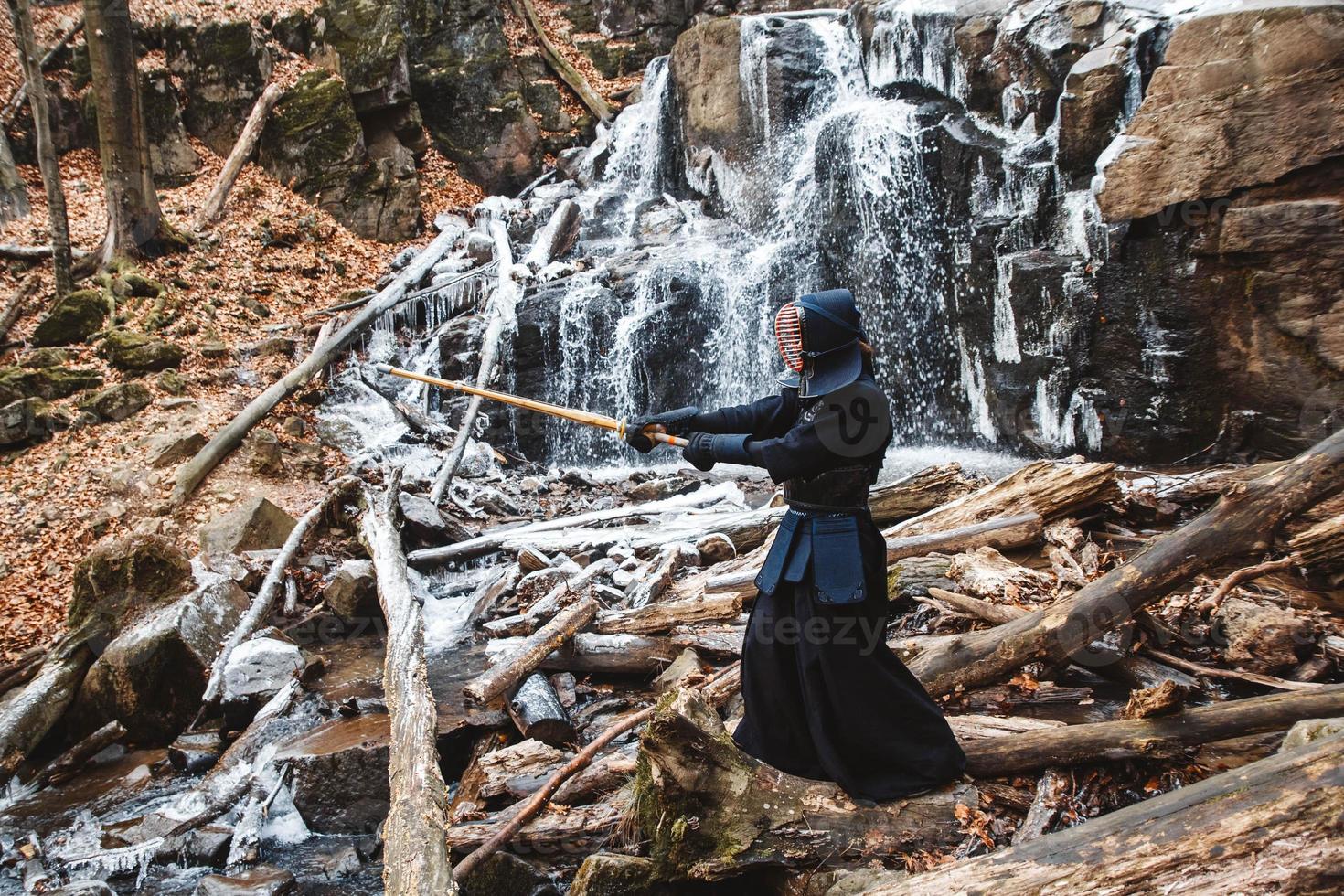 Man practicing kendo with bamboo sword on waterfall background photo