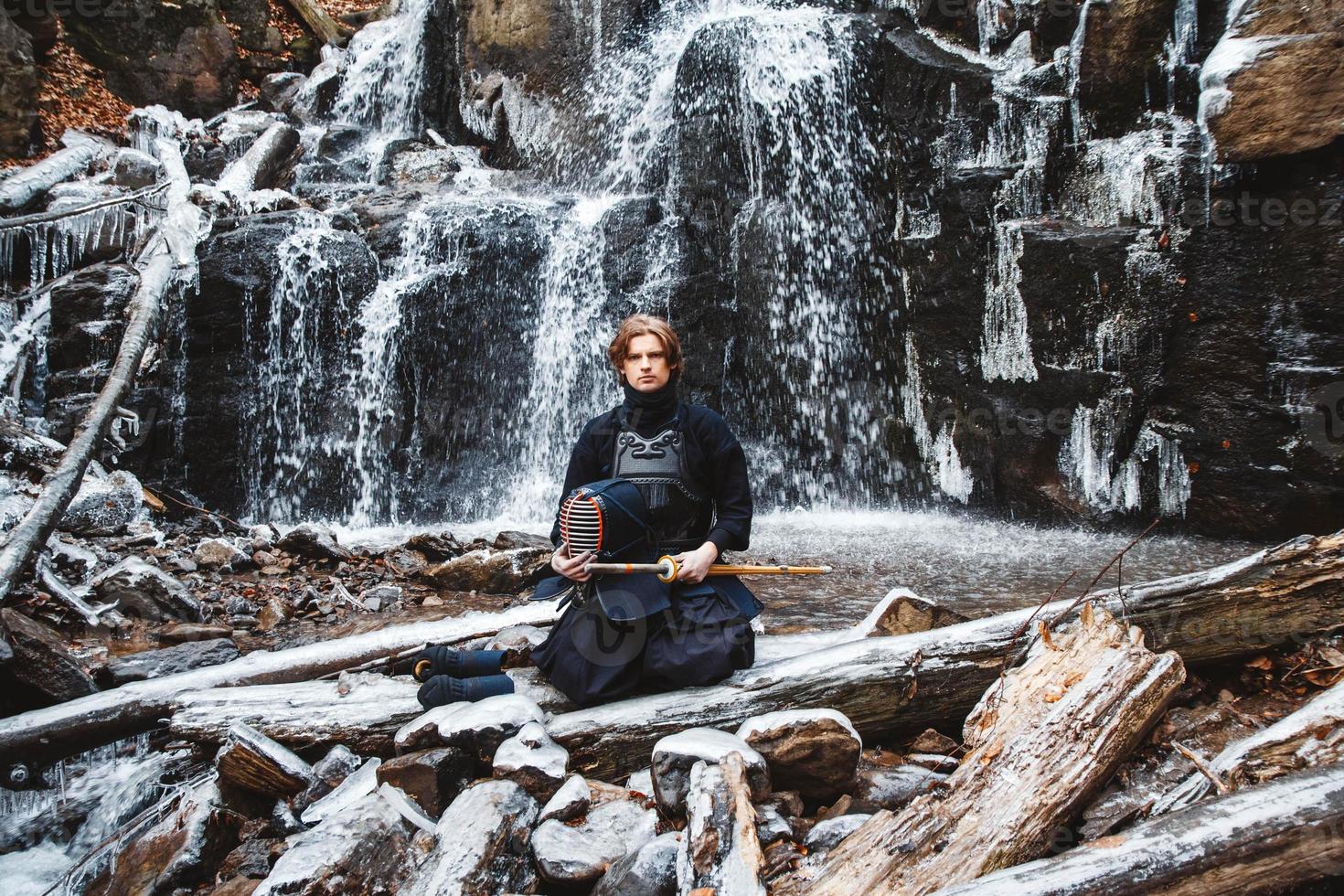 Man practicing kendo with bamboo sword on waterfall background photo
