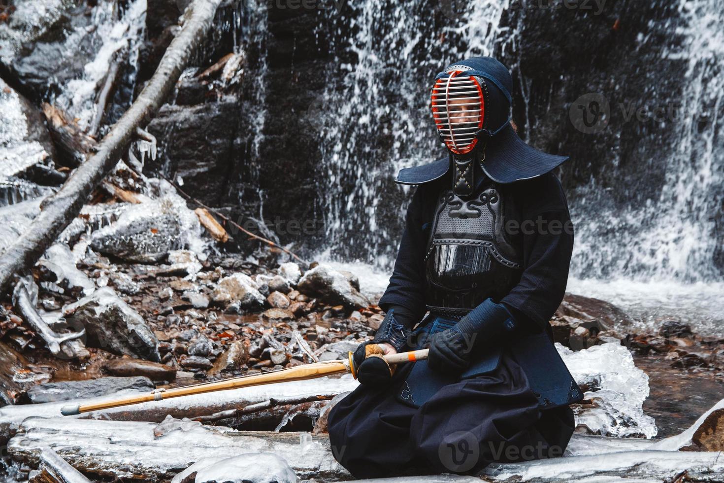 Man practicing kendo with bamboo sword on waterfall background photo