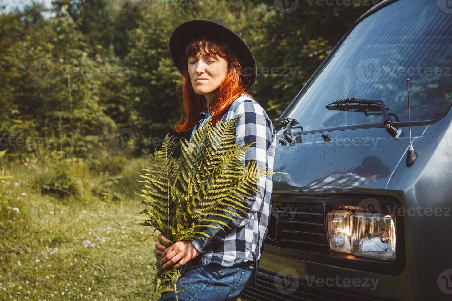 Woman in hat holding fern leaves standing near the van on background of green grass photo