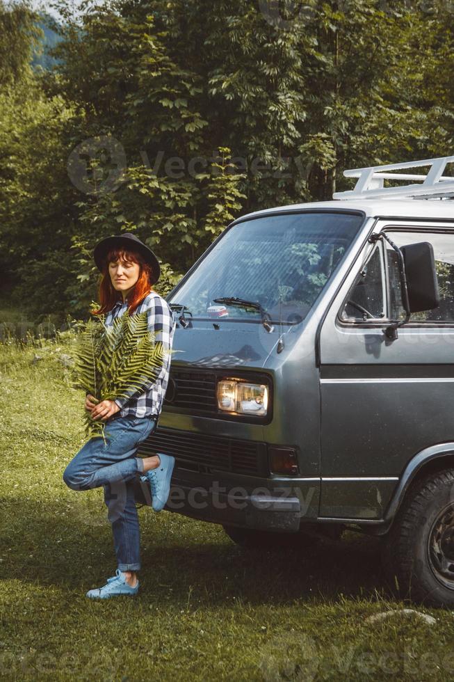 Woman in hat holding fern leaves standing near the van on background of green grass photo