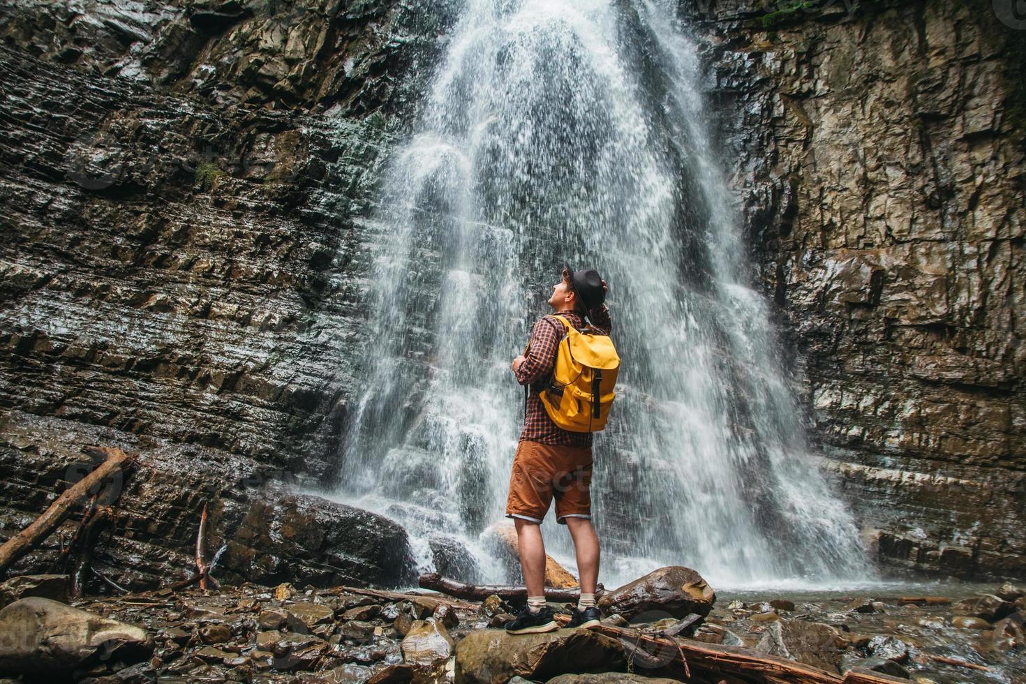 Hombre con una mochila amarilla de pie sobre el fondo de una cascada foto