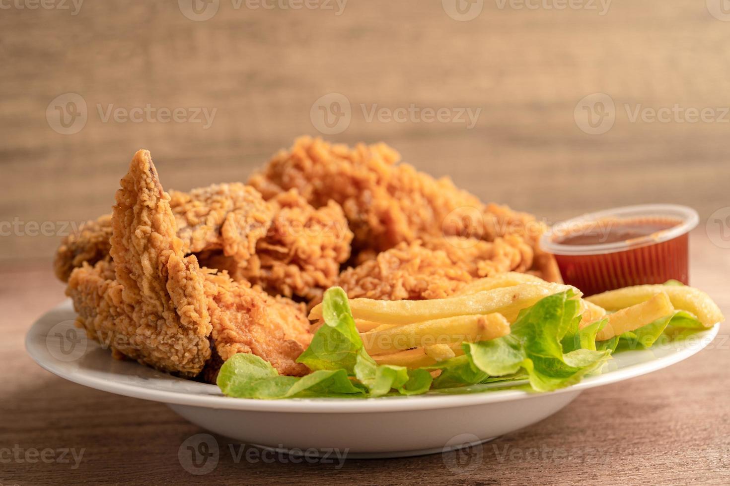 Pollo frito y papas fritas con hojas de romero, comida chatarra alta en calorías servida en un plato blanco foto