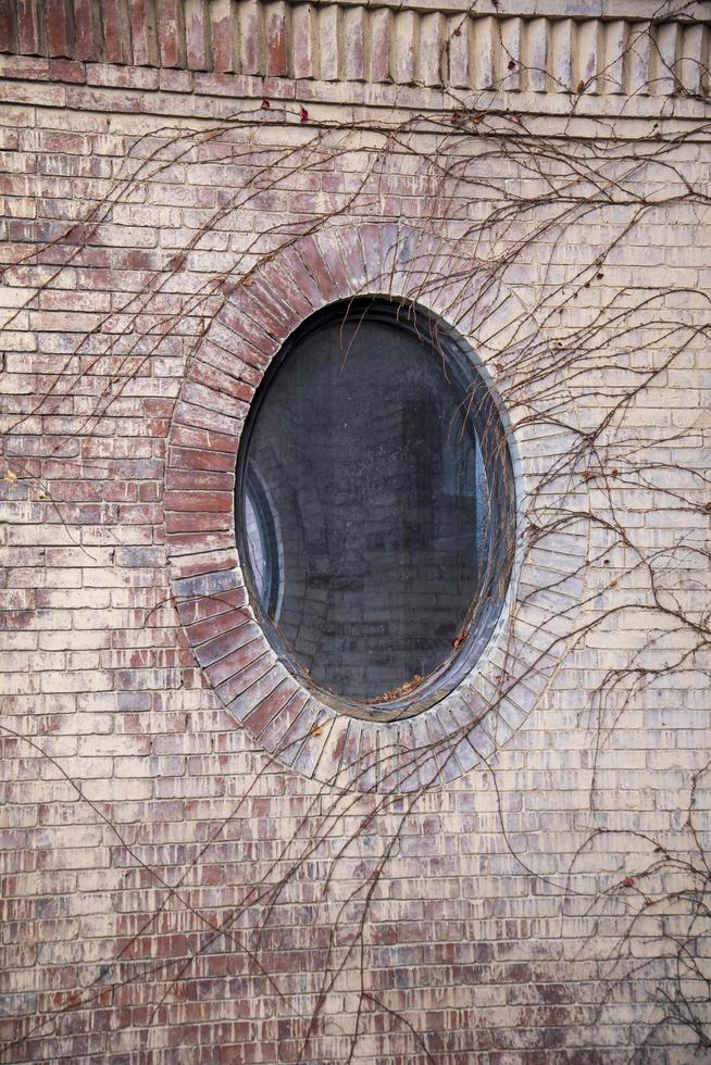 Ventana circular en el lateral de un edificio de ladrillo rodeado de hiedra foto