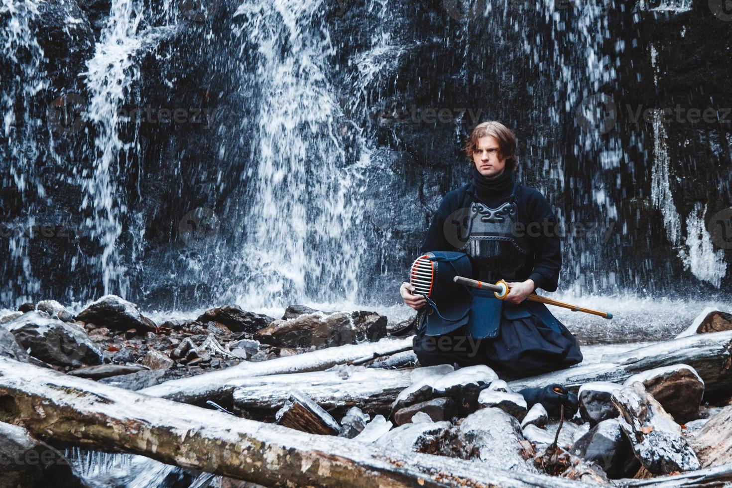 Hombre practicando kendo con espada de bambú sobre fondo de cascada foto