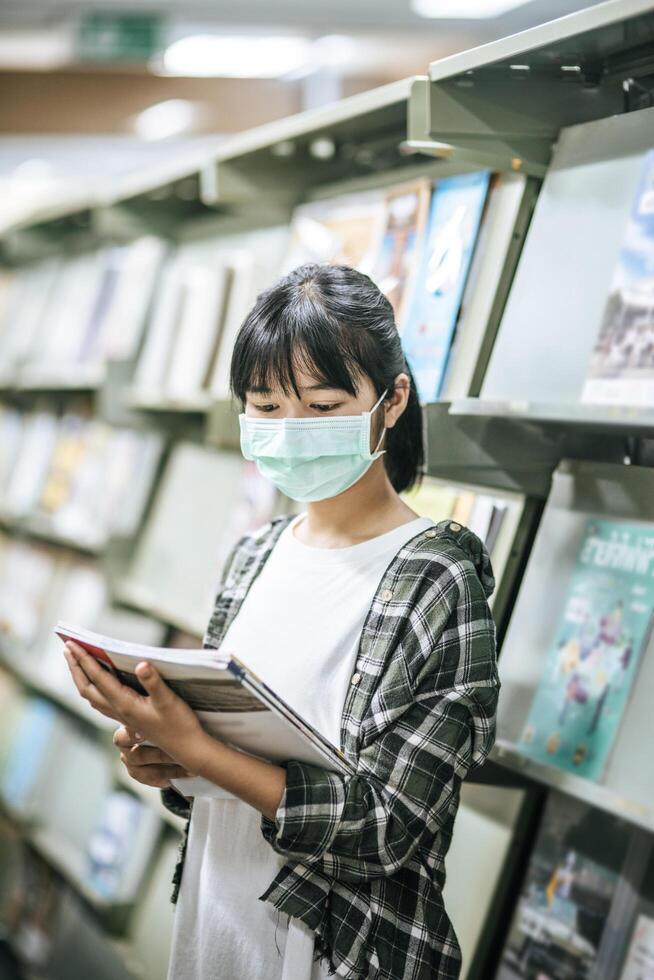 una mujer con una máscara y buscando libros en la biblioteca. foto