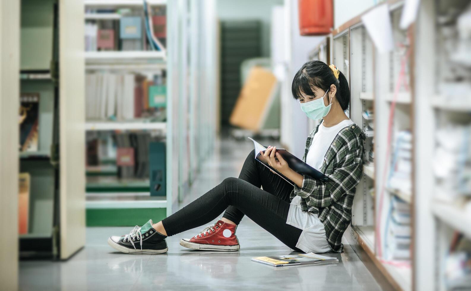 una mujer con máscaras está sentada leyendo un libro en la biblioteca. foto