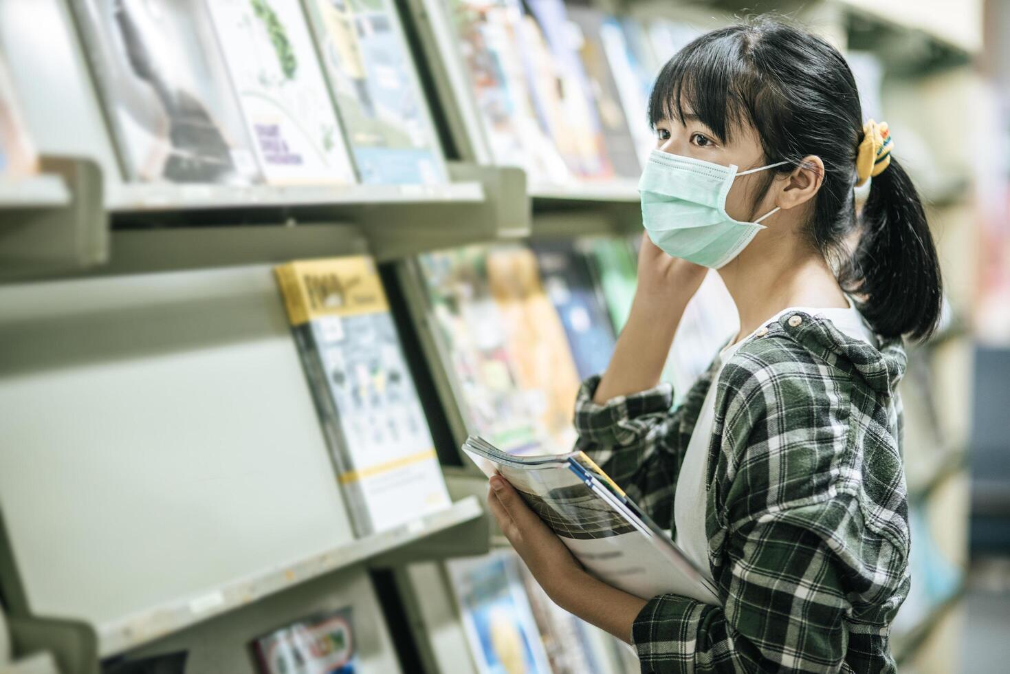 A woman wearing a mask and searching for books in the library. photo