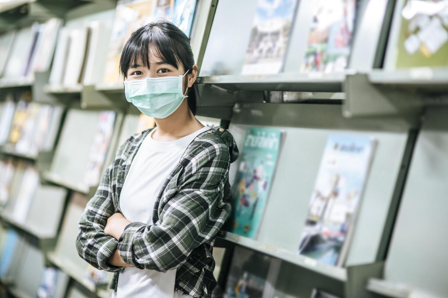 A woman wearing a mask and searching for books in the library. photo