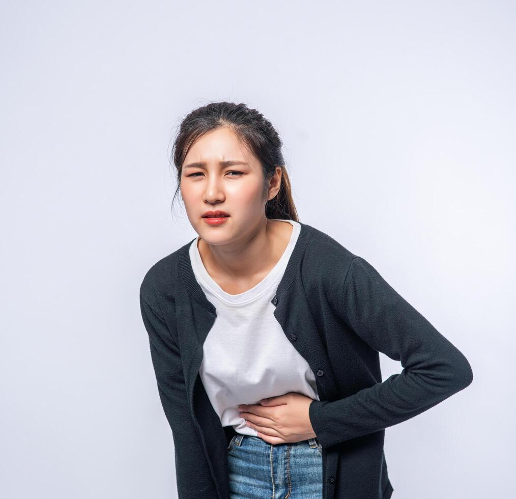 A woman standing with a stomach ache and presses her hand on her stomach. photo